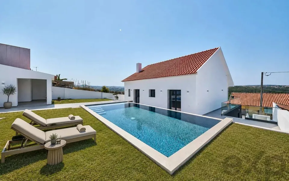 Moradia branca de telhado de telha na Ericeira, com piscina de bordo transbordante, relvado e espreguiçadeiras